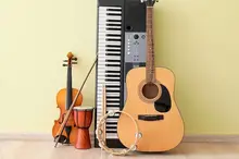 En gitarr, fiol, keyboard och tambourine står lutade mot en grön vägg