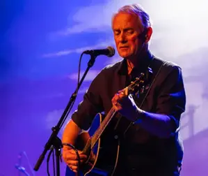 En man som spelar gitarr och sjunger i en mikrofon.
