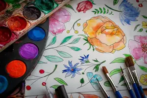 Penslar och färgpaletter bredvid en teckning med blommor.