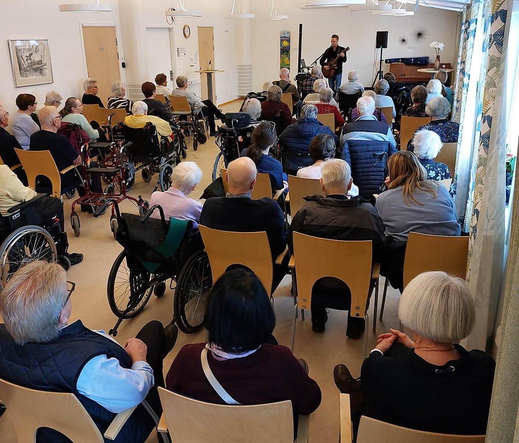 Lokal Bergtet på Götene Äldreceneter är fylld av publik och musiker Henrik Strömberg spelar gitarr.